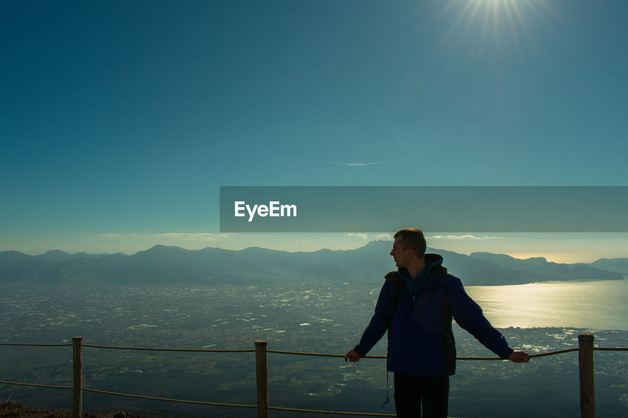 Young man standing on observation point against blue sky during sunset