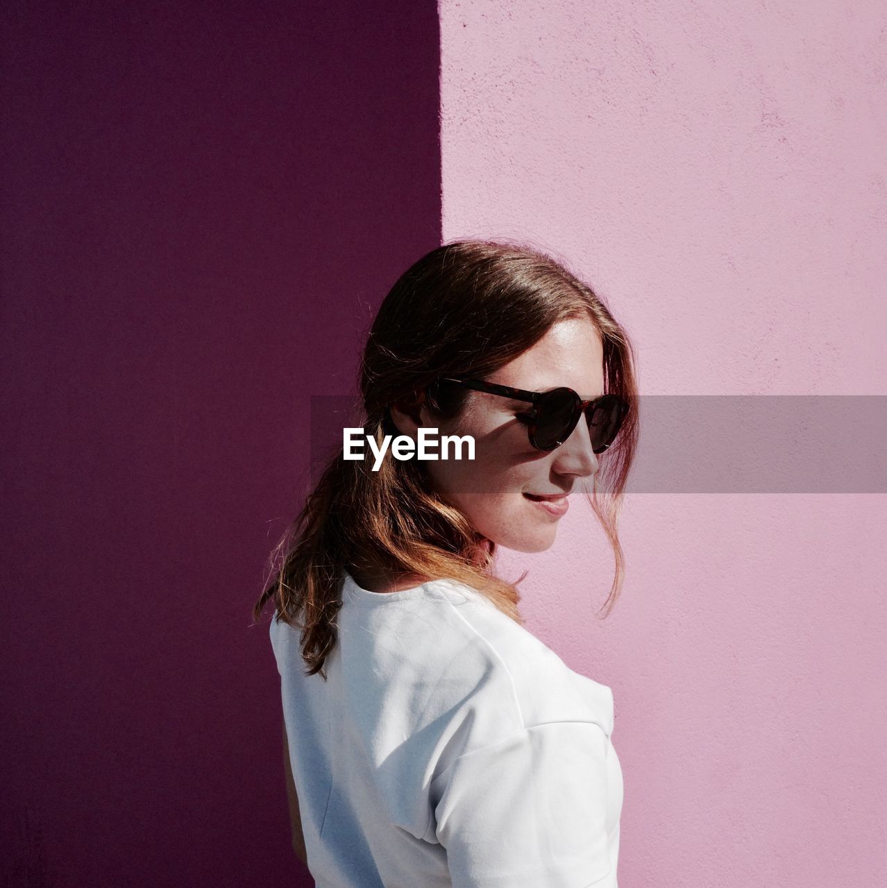 Smiling woman wearing sunglasses while standing against pink wall