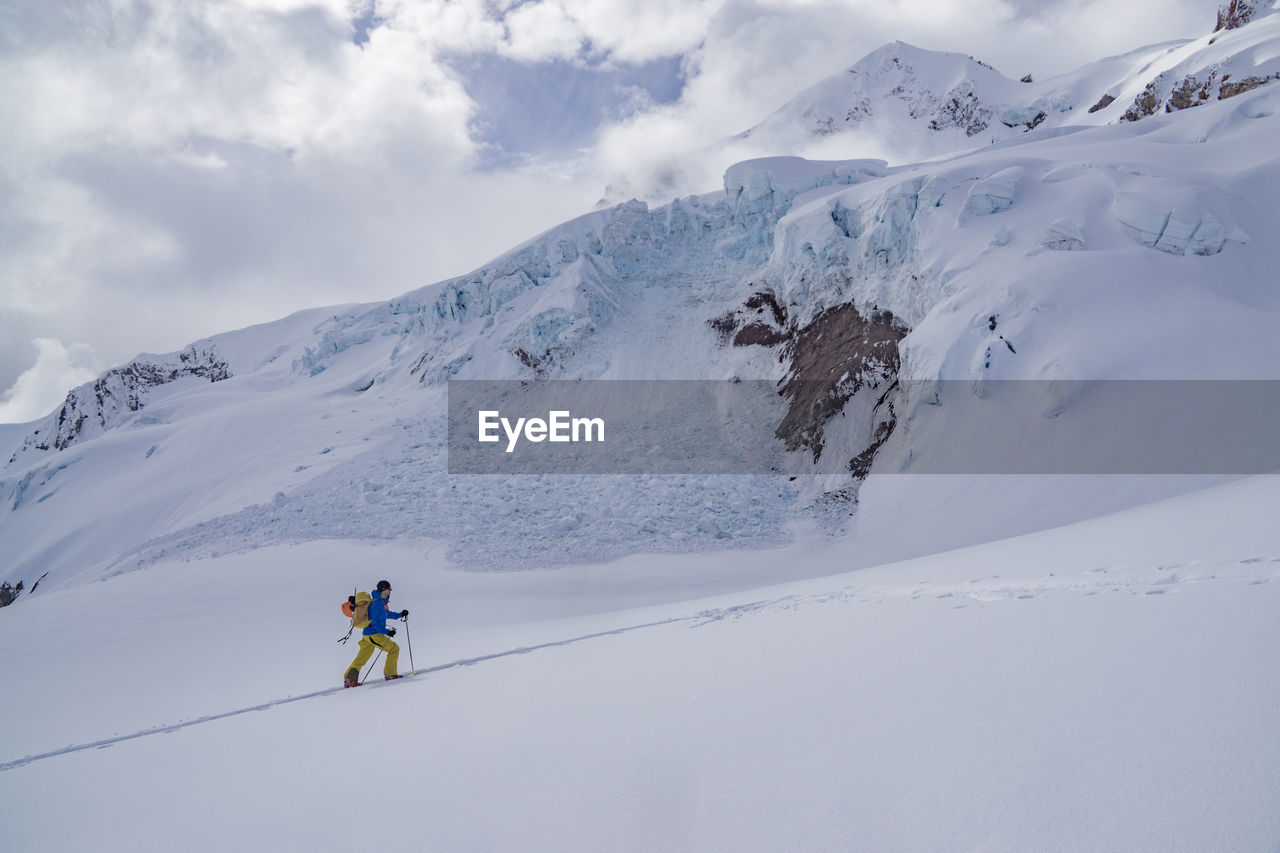 Man climbing on snow covered mountain against sky