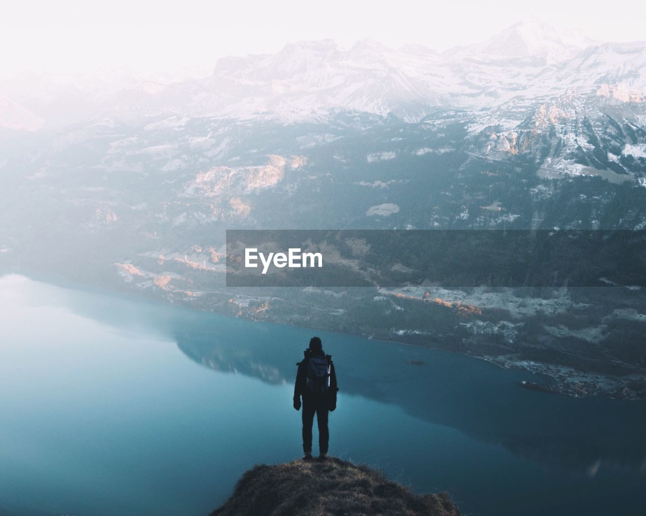 REAR VIEW OF MAN LOOKING AT LAKE AGAINST MOUNTAIN