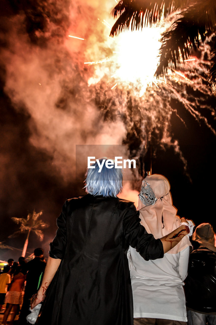 Rear view of young couple standing against firework display in sky at night