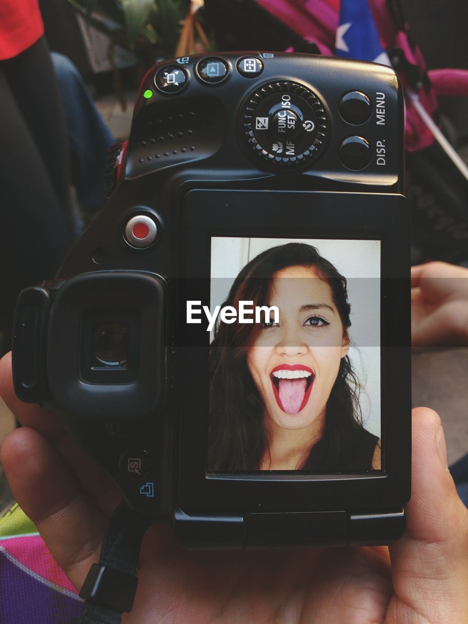 Cropped image of hand holding camera with woman sticking out tongue on screen