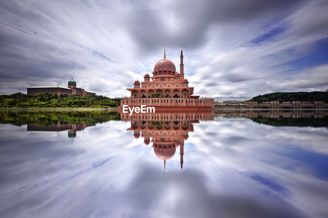 Mosque reflecting in lake against cloudy sky