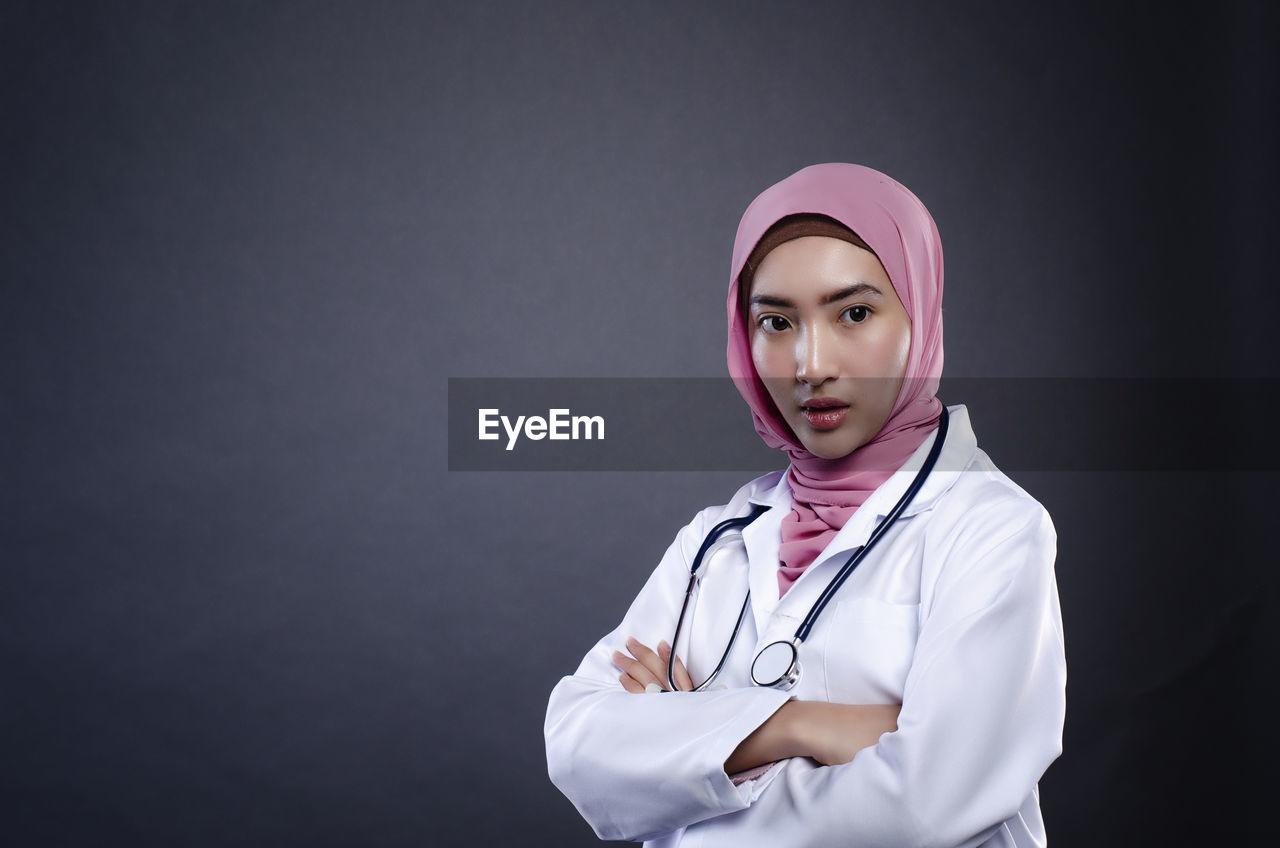 Portrait of doctor standing against gray background