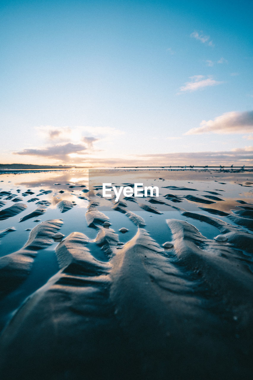 Surface level of beach against sky during sunset