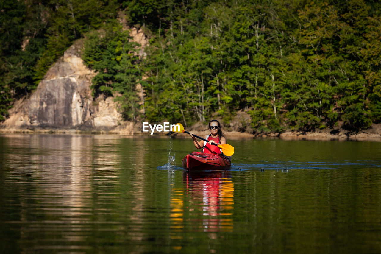 Man sitting in boat on lake against trees