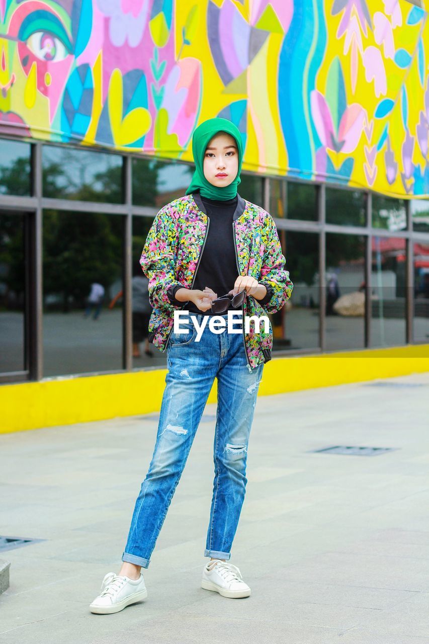 Full length of young woman hijab standing against wall