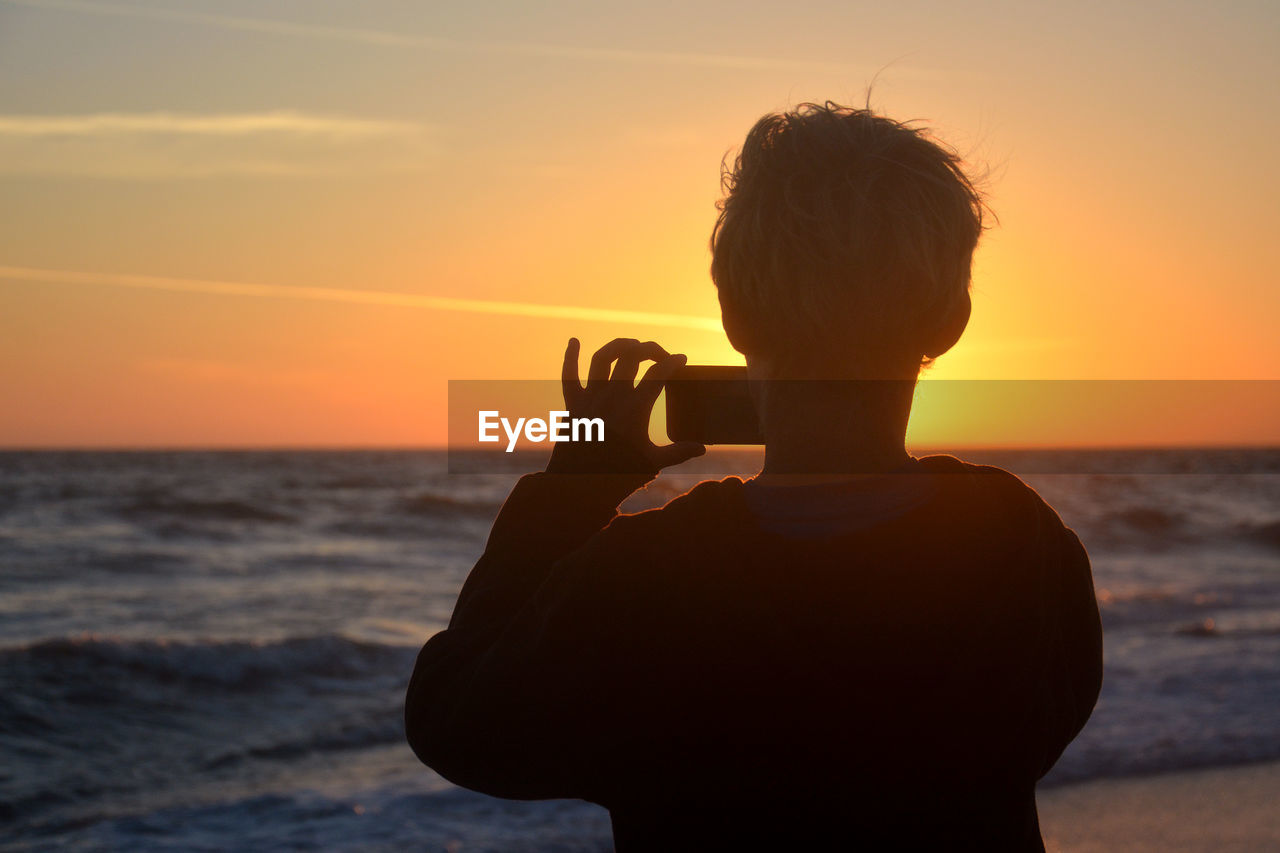 Rear view of silhouette man standing at beach during sunset