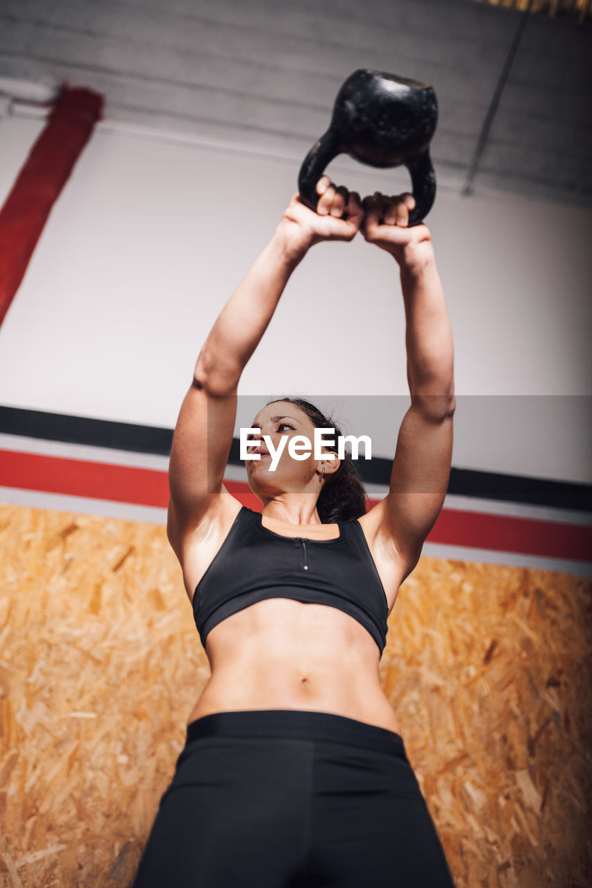 MIDSECTION OF WOMAN HOLDING CAMERA WHILE SITTING ON WALL