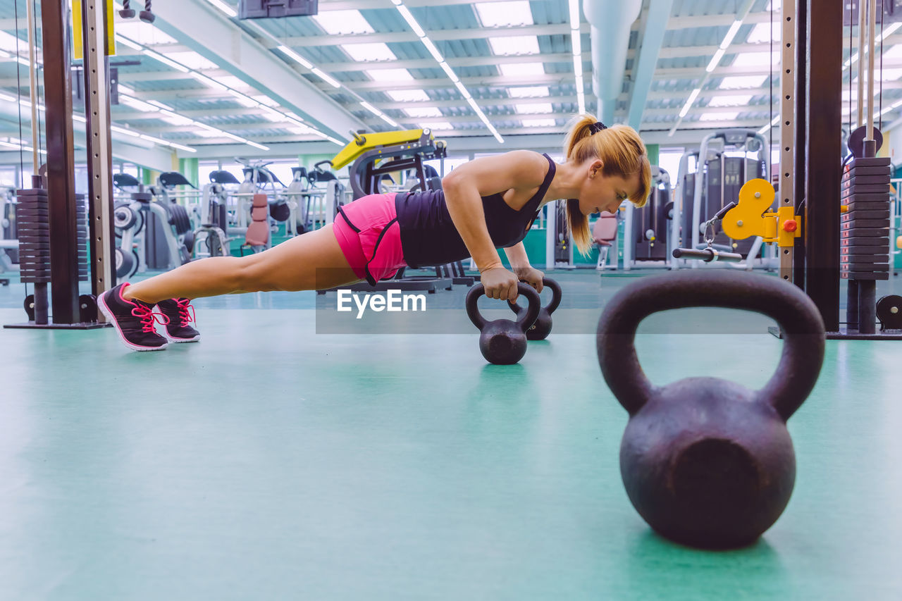 Full length of woman doing push-ups with kettlebell at gym