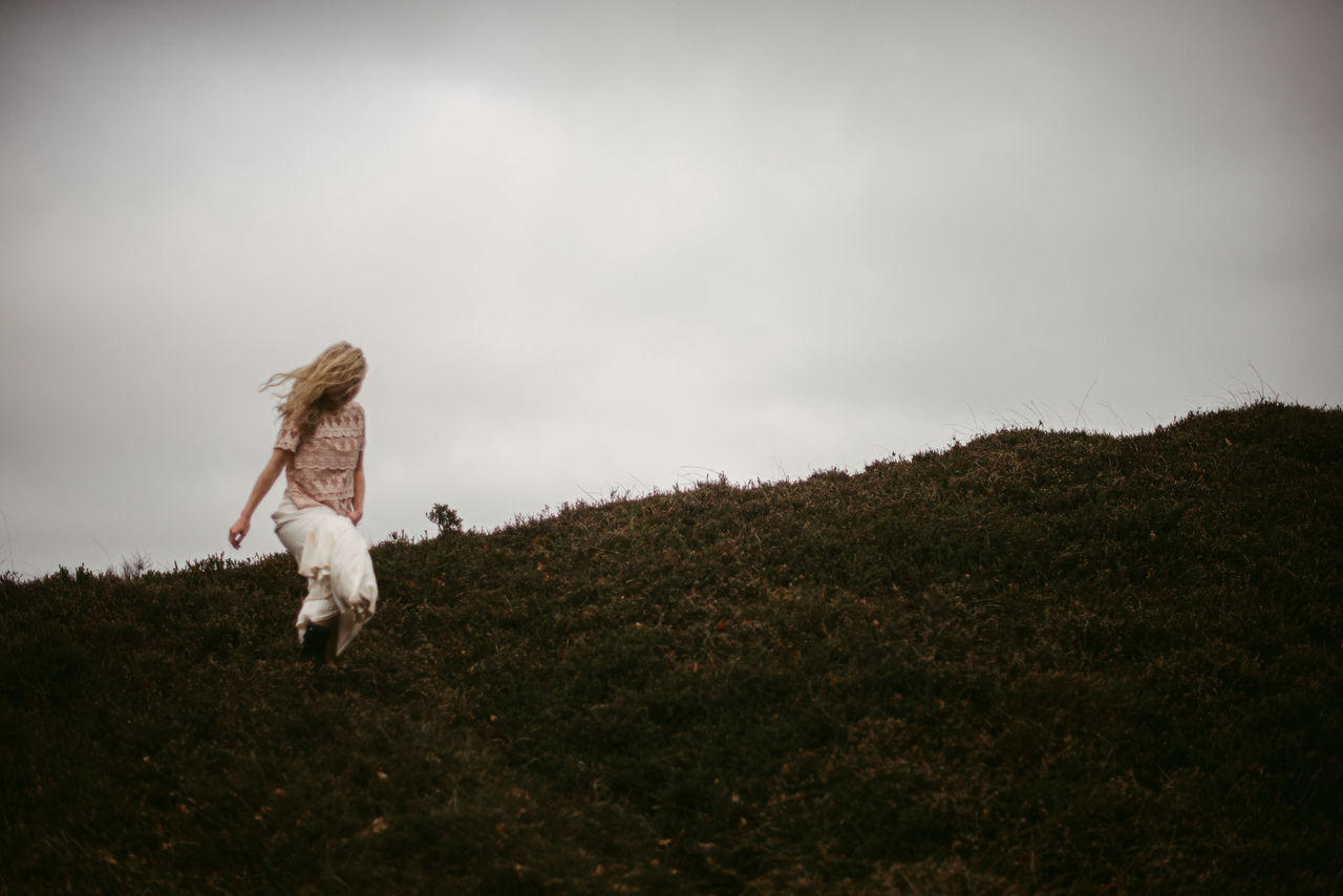 WOMAN RUNNING ON FIELD BY ROCK AGAINST SKY