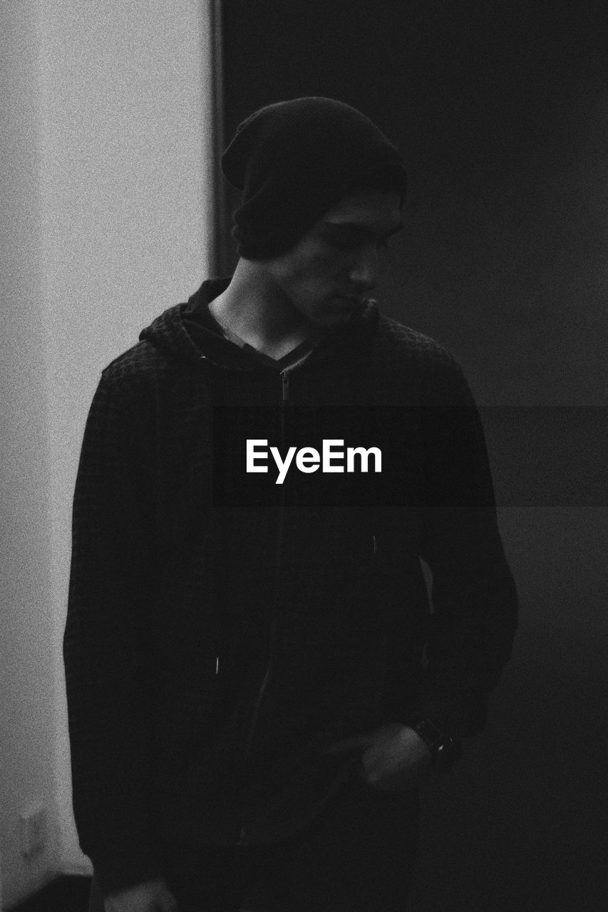 Young man looking away while standing against wall