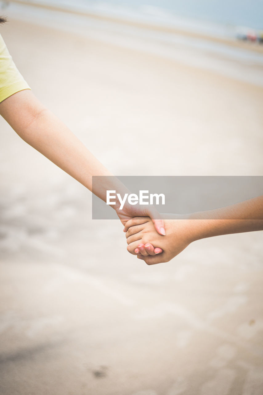 hand, holding hands, adult, women, togetherness, limb, two people, nature, land, beach, positive emotion, human limb, close-up, love, human leg, emotion, focus on foreground, arm, day, sea, person, young adult, skin, water, sand, outdoors, holiday, sky, vacation, yellow, trip, female, lifestyles, relaxation, bonding, copy space, leisure activity, clothing