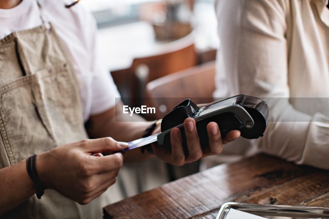 Owner using credit card reader while standing by male customer at table