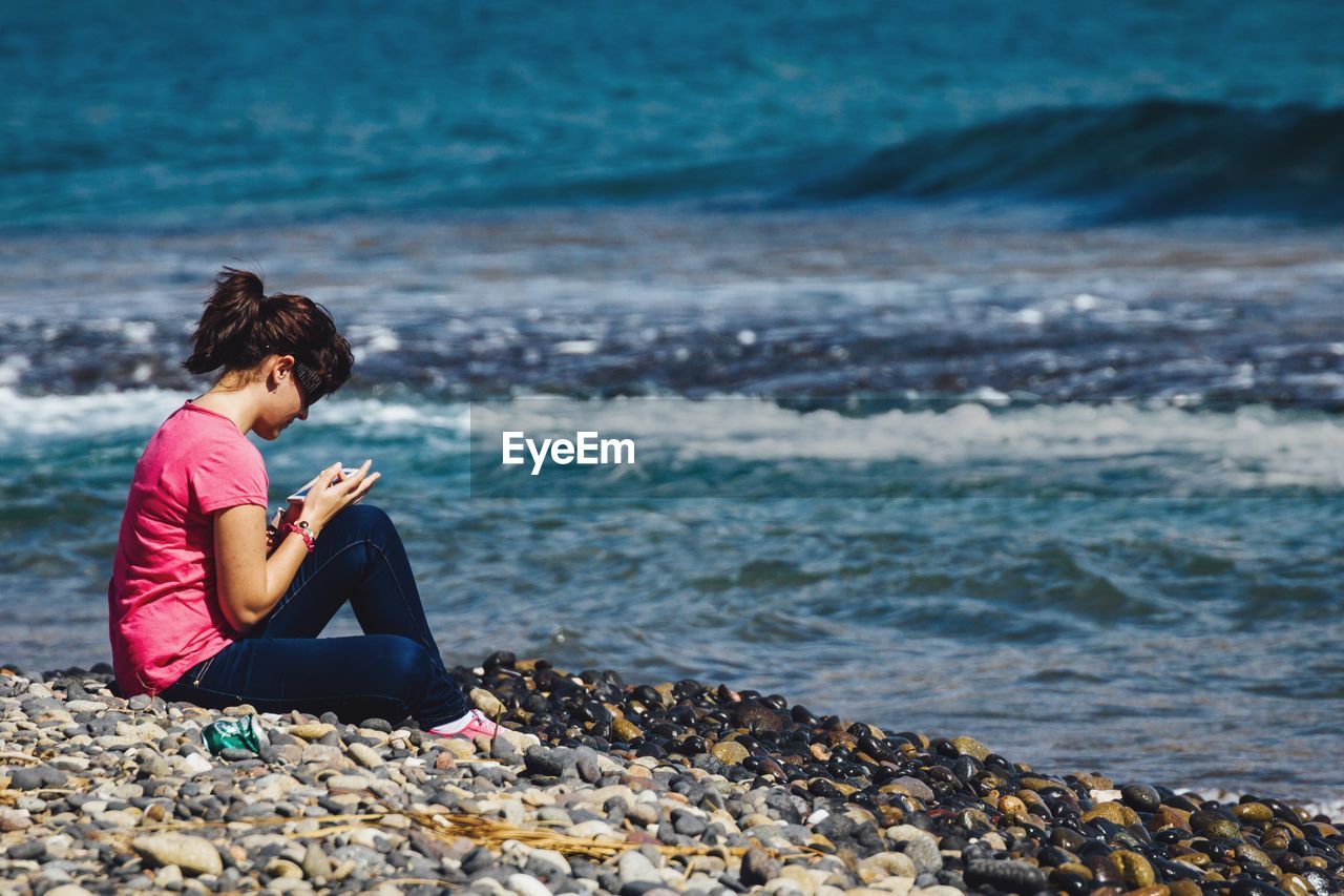 Rear view of woman sitting on rocks at beach