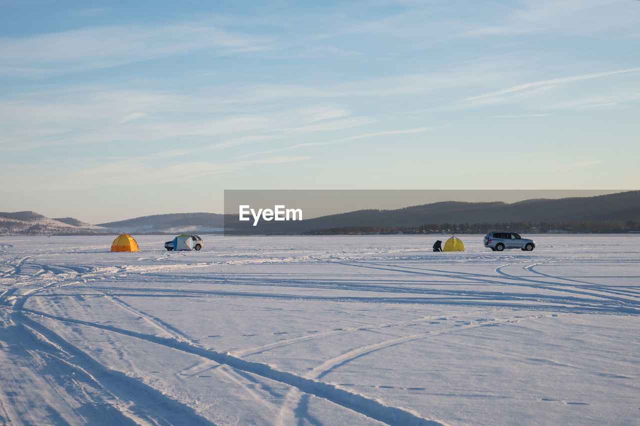 Winter lake with tents and cars of fishermens against the background of mountains.