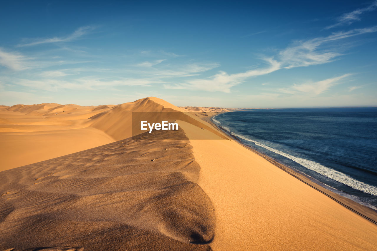 Scenic view of sand dunes by sea against blue sky