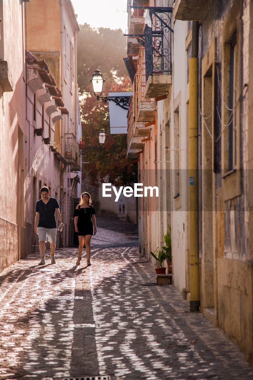 REAR VIEW OF PEOPLE WALKING ON COBBLESTONE STREET