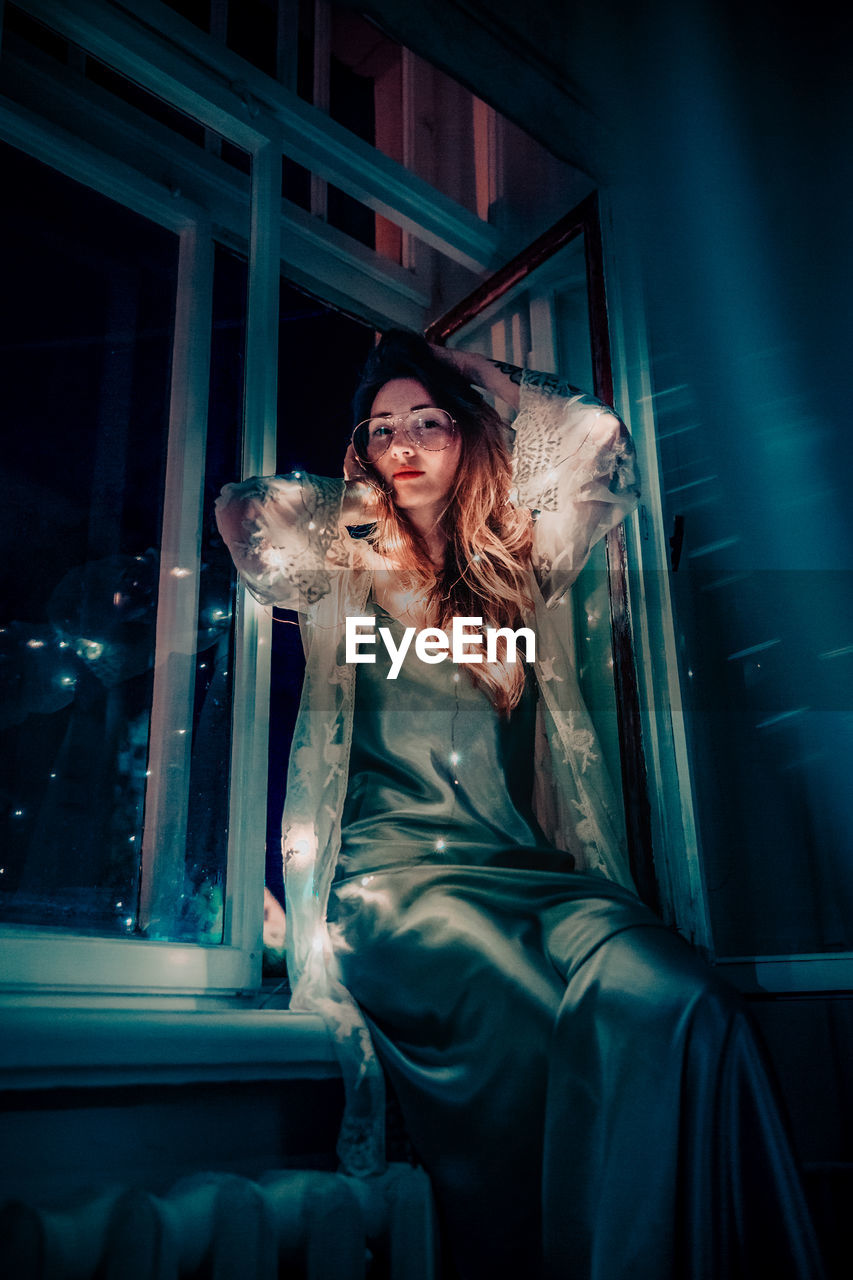 Portrait of woman with illuminated string light sitting on window sill