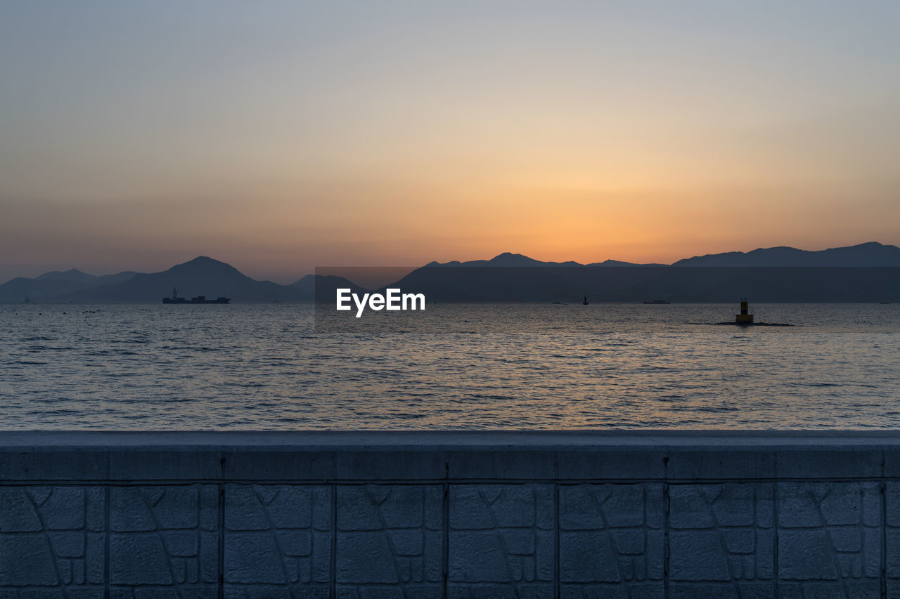 Scenic view of sea by mountains against sky during sunset