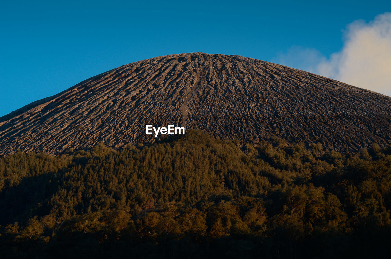 Low angle view of volcanic mountain against blue sky