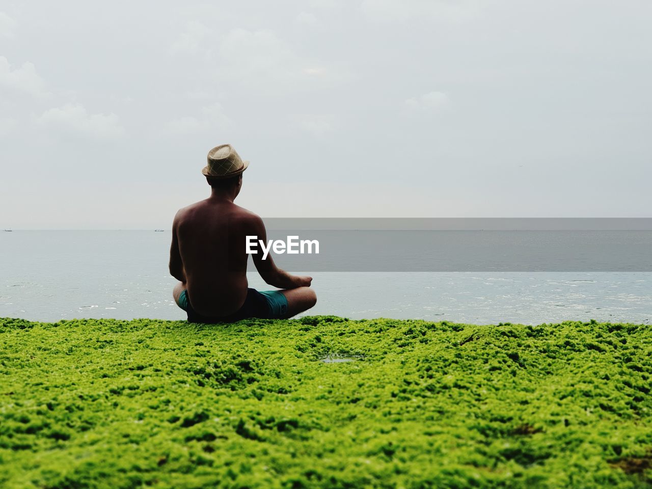 Rear view of man meditating while sitting by sea against sky