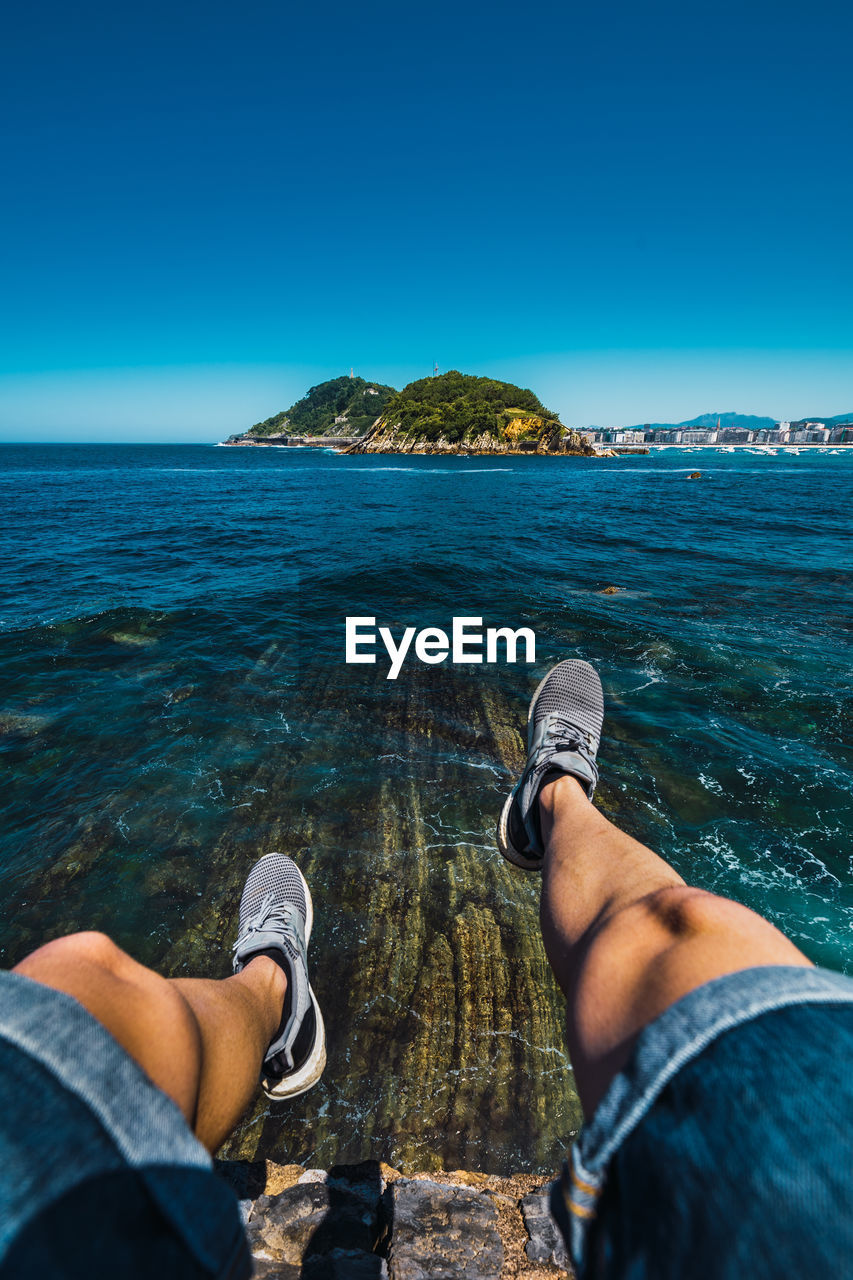 From above of crop unrecognizable tourist admiring ocean from mount under cloudless sky in basque country