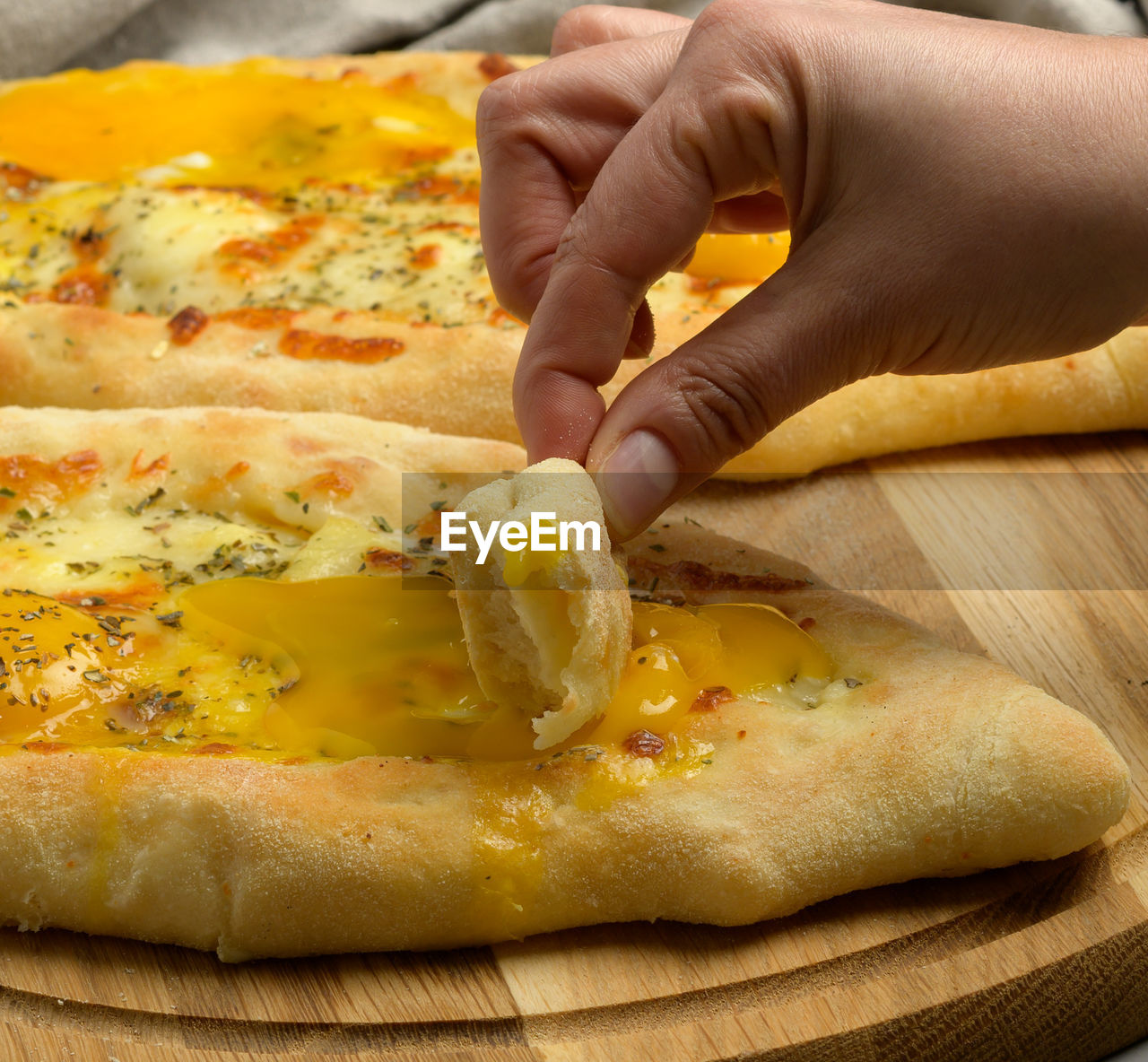 Baked adjarian khachapuri with whole egg yolk on a wooden board, hand beats a piece of bread 