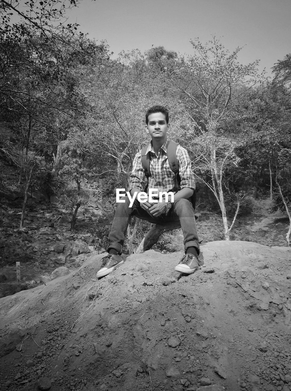 Portrait of young man sitting on rock against trees in forest