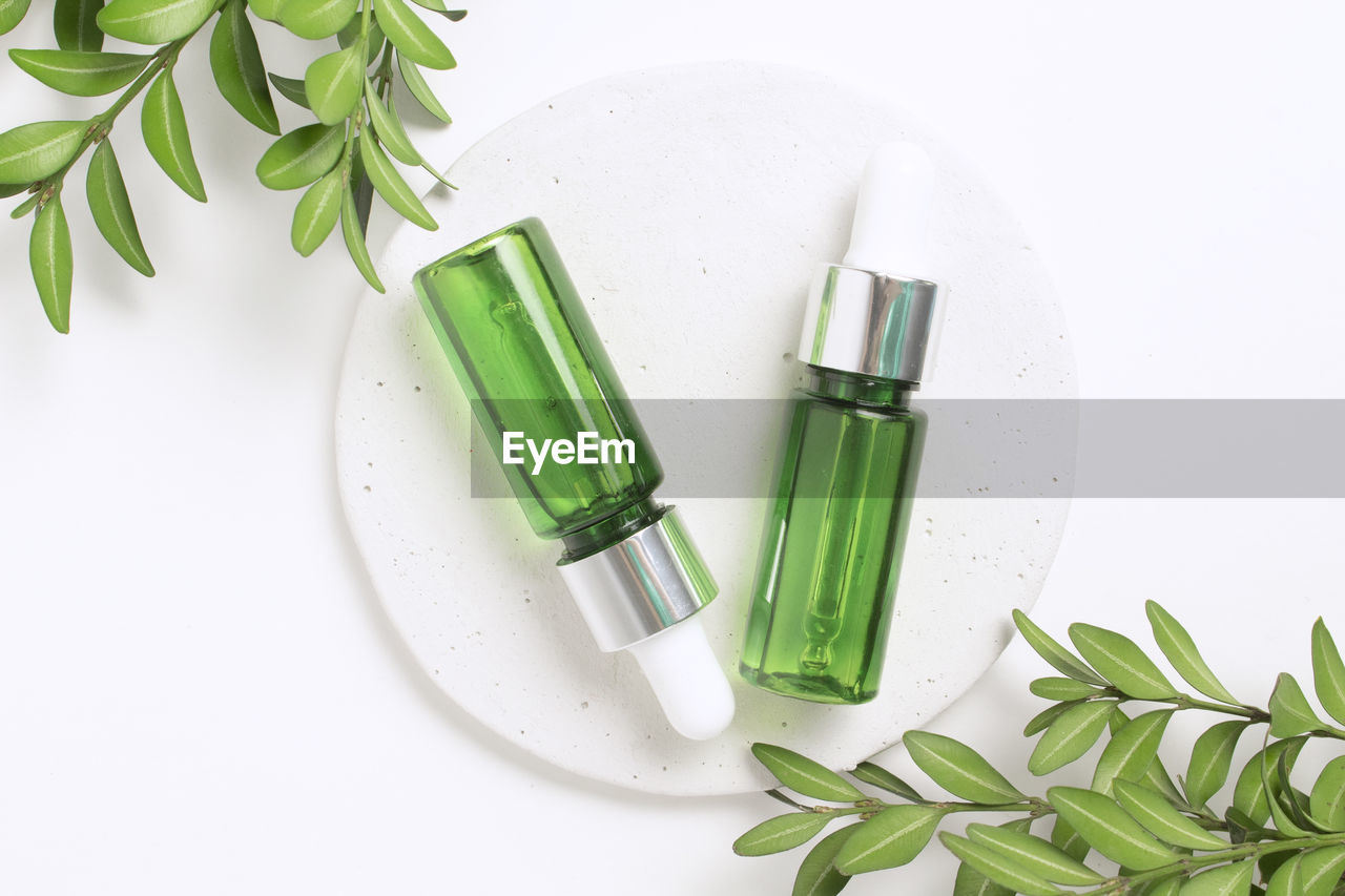 Green glass dropper bottles on concrete podium with leaves. cosmetic container mock-up
