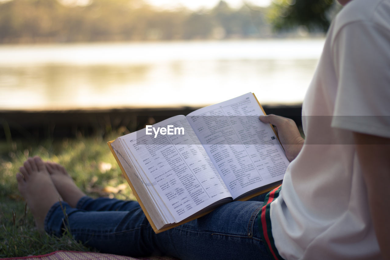 Low section of woman reading book at park