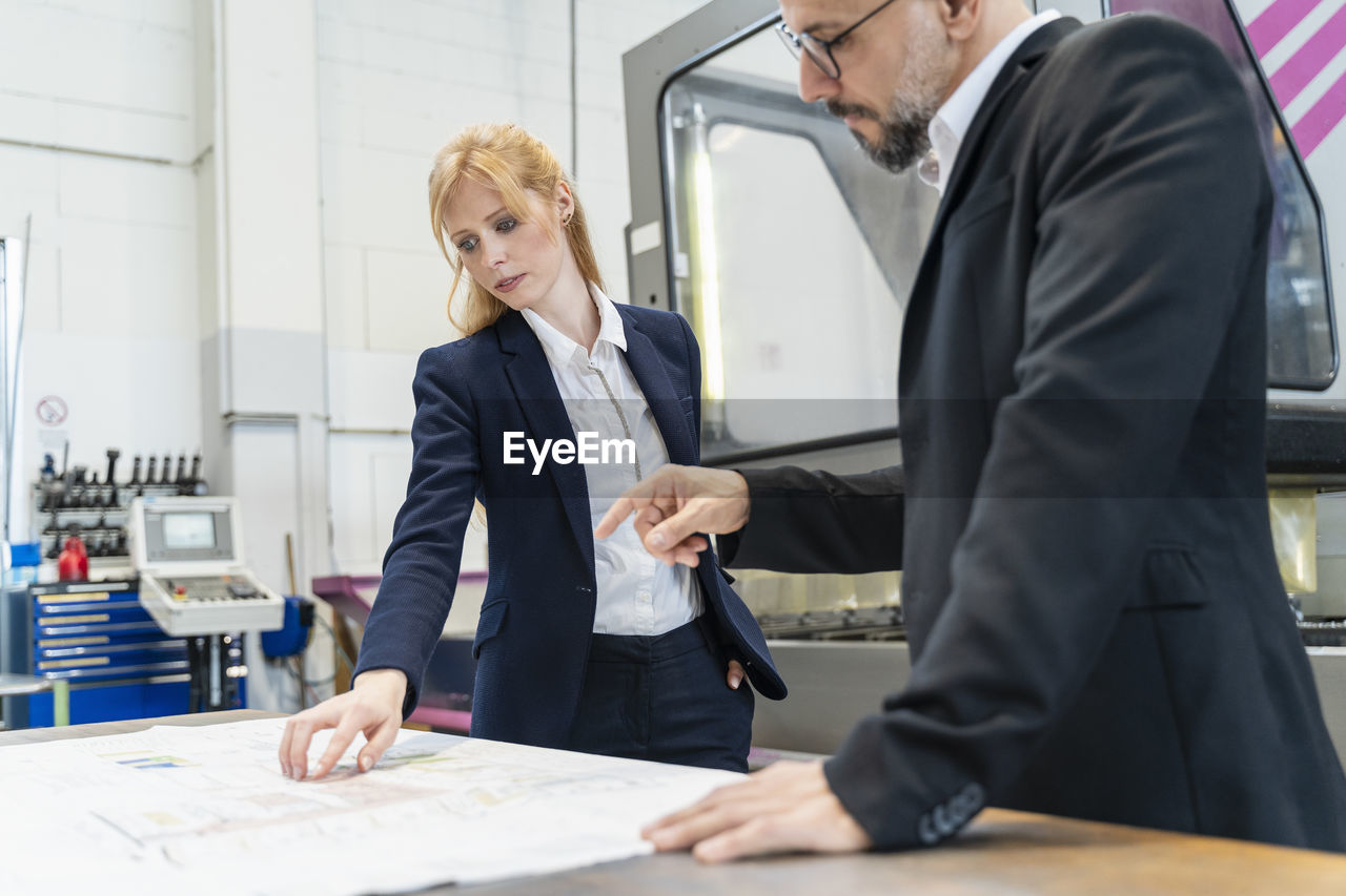 Businessman and businesswoman looking at plan on table in factory