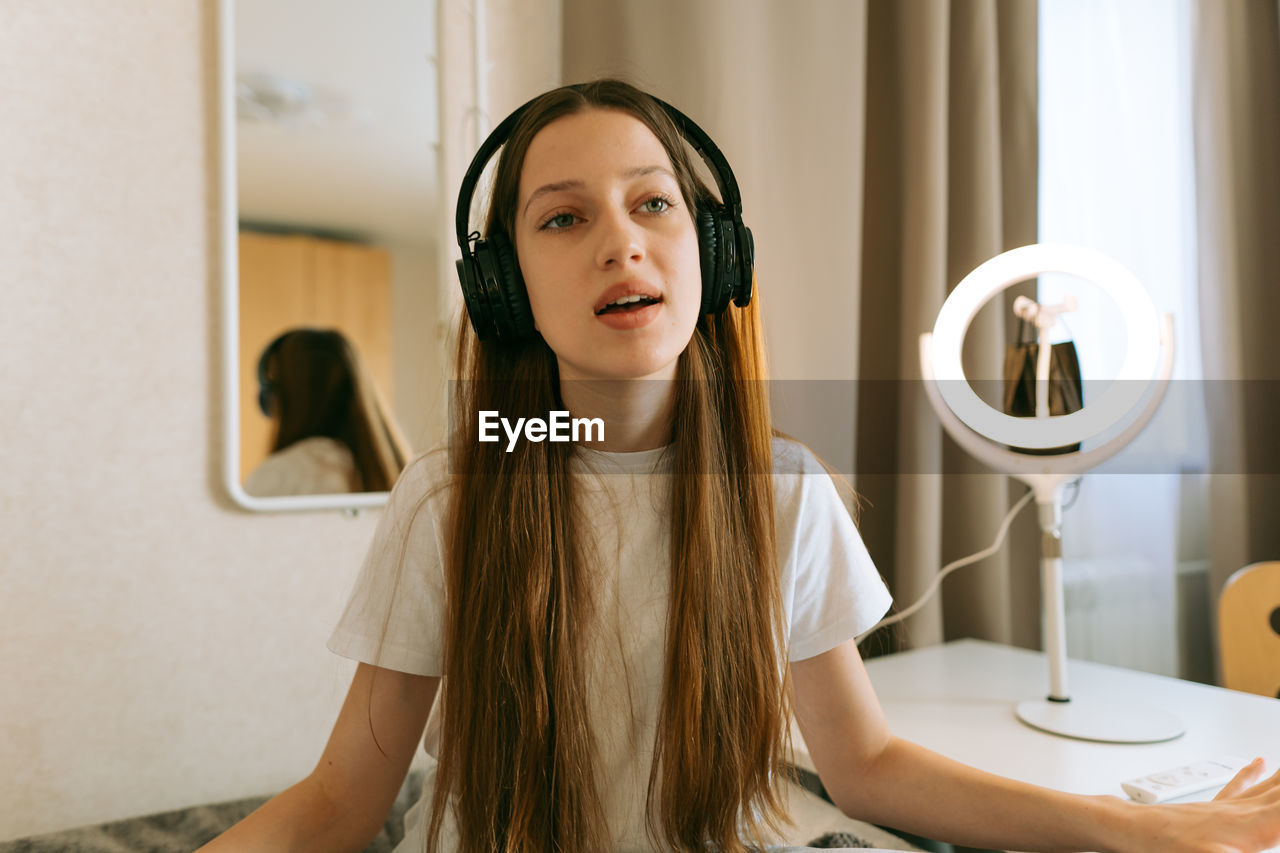 Teenage girl wearing wireless headphones sitting at home