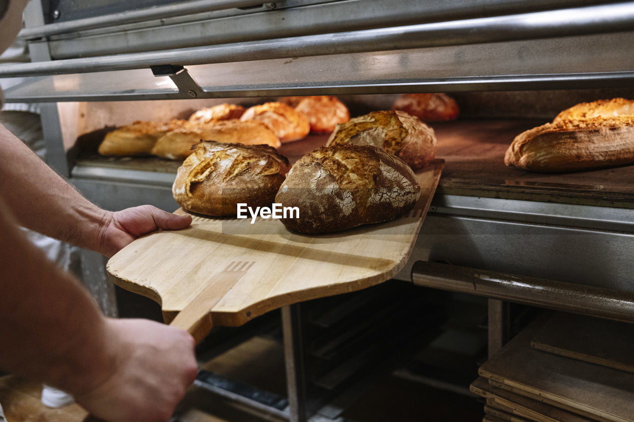 Male chef with pizza peel removing baked bread from oven at bakery