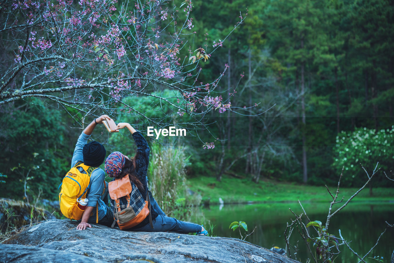 Rear view of couple sitting by lake on rock at forest