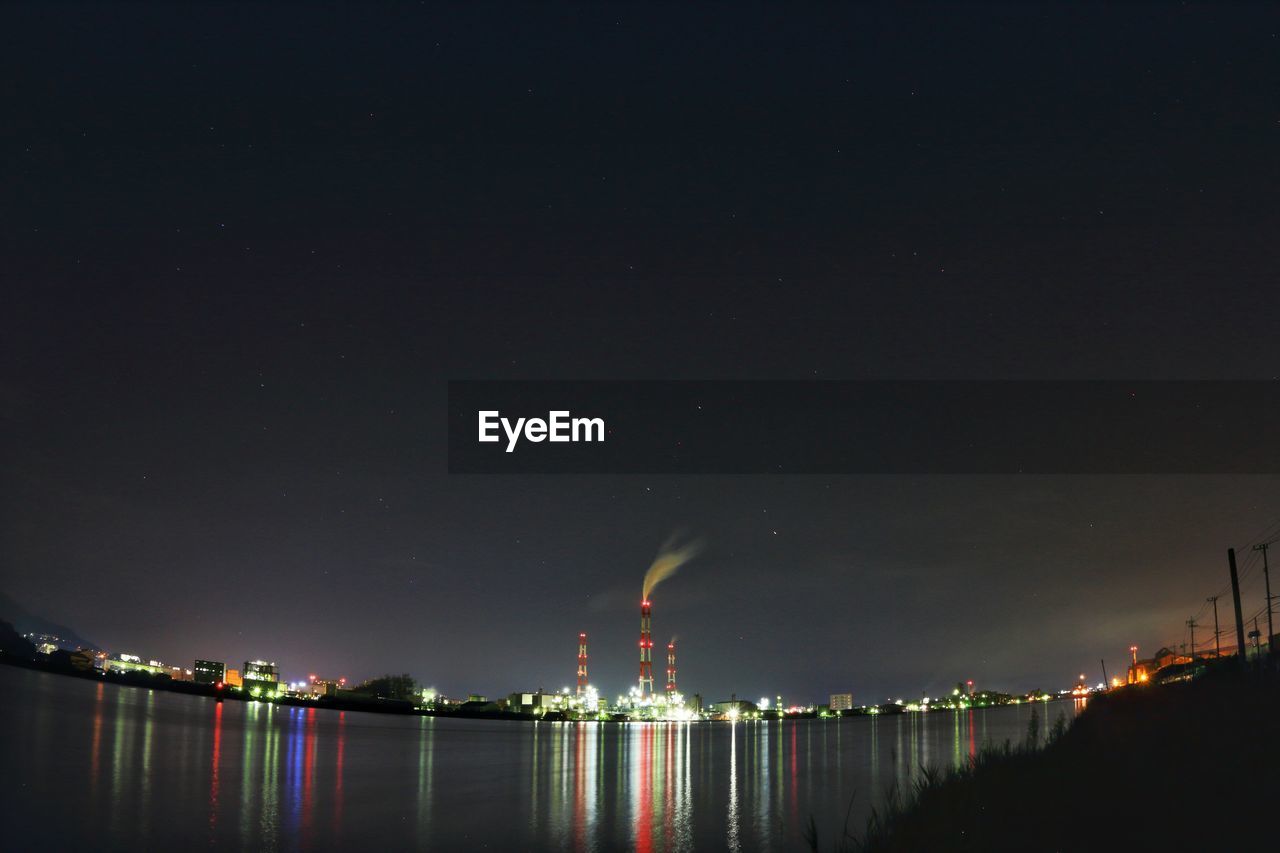 Illuminated industrial buildings and smoke stacks by river at night