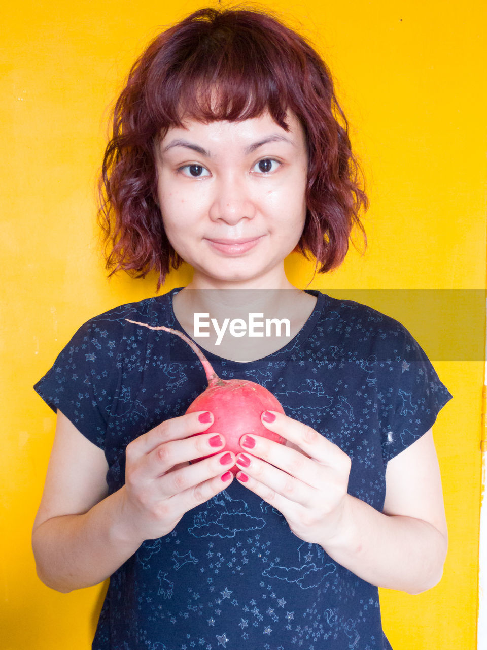 Portrait of woman holding radish against yellow background