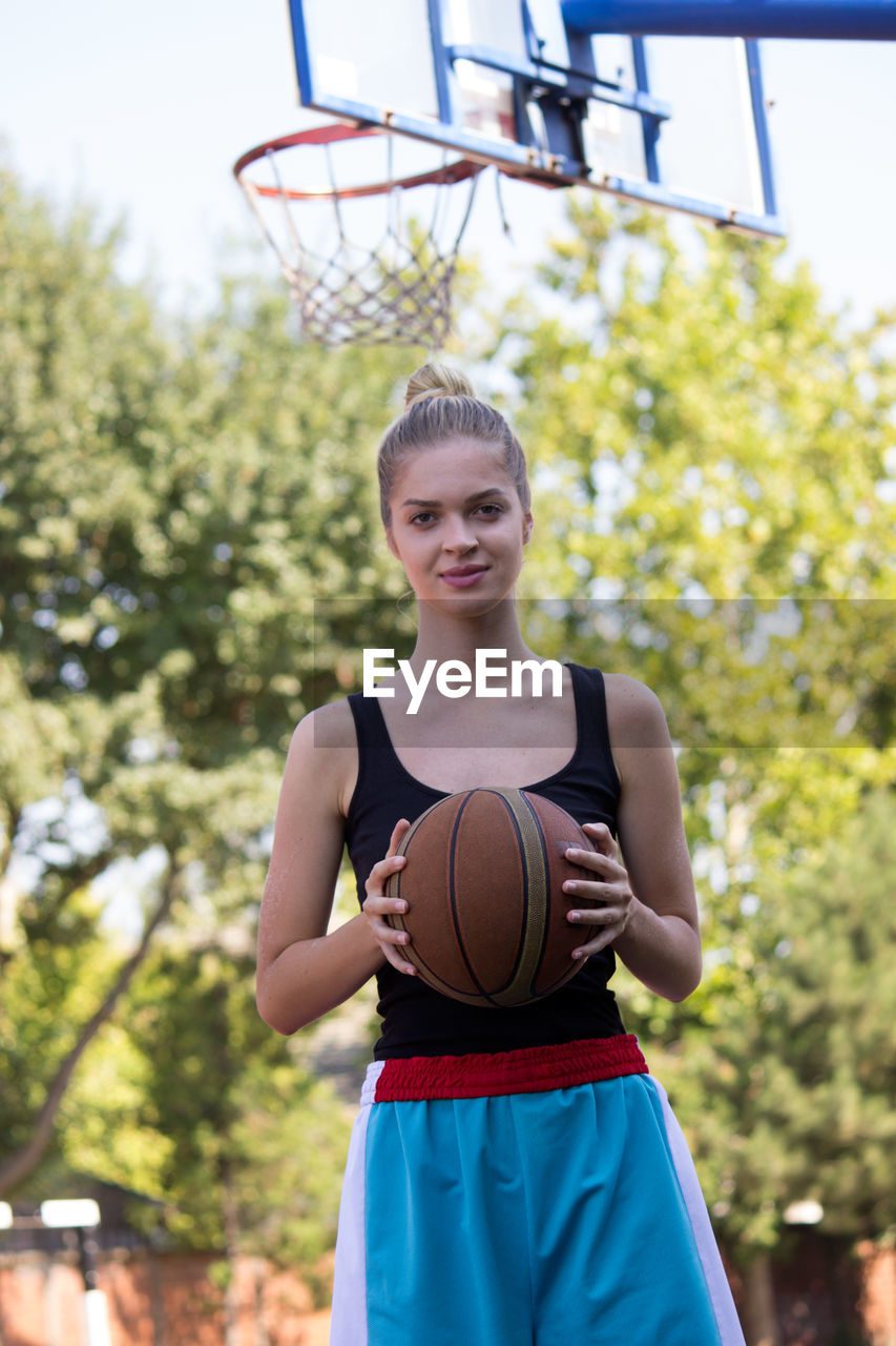 Portrait of young woman holding basketball in court