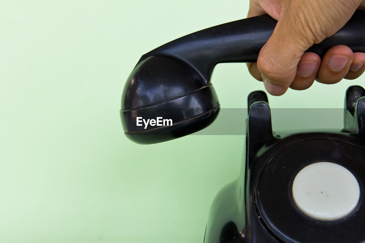 Close-up of hand holding telephone receiver against green background