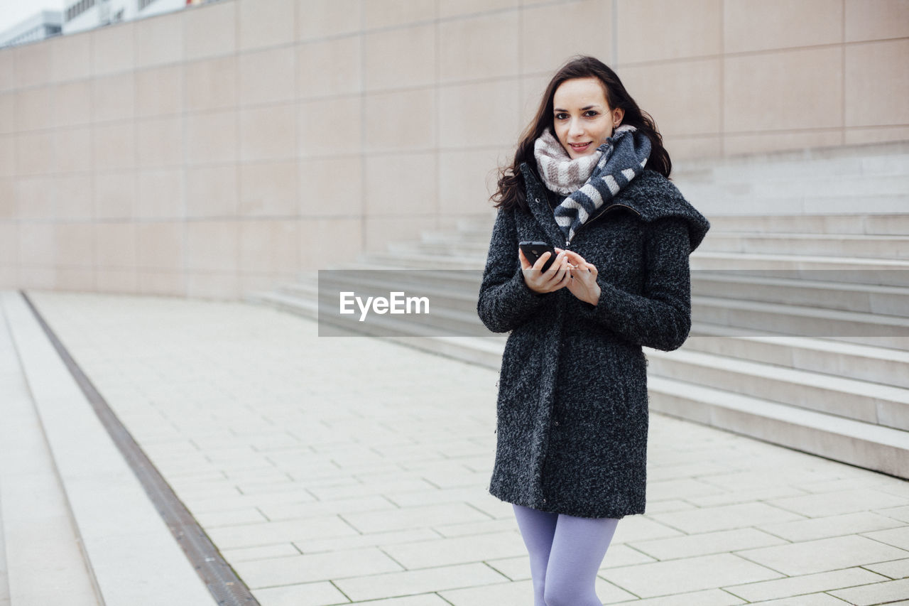 Portrait of beautiful young woman using phone on footpath