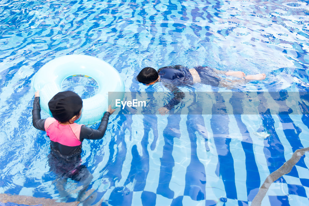 REAR VIEW OF WOMEN SWIMMING IN POOL