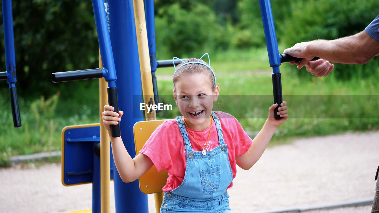 Smiling, happy eight year old girl engaged, doing exercises on outdoor exercise equipment