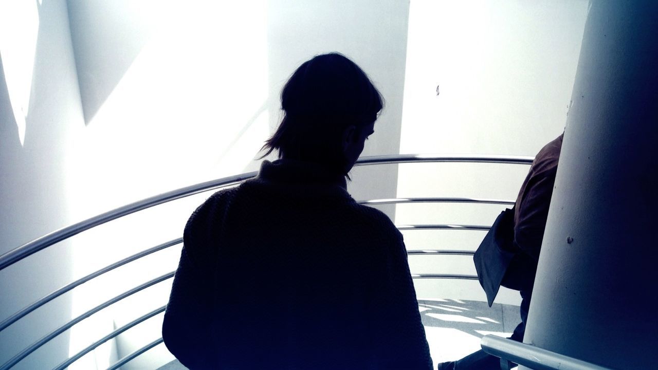 Rear view of a silhouette man against railing and white wall