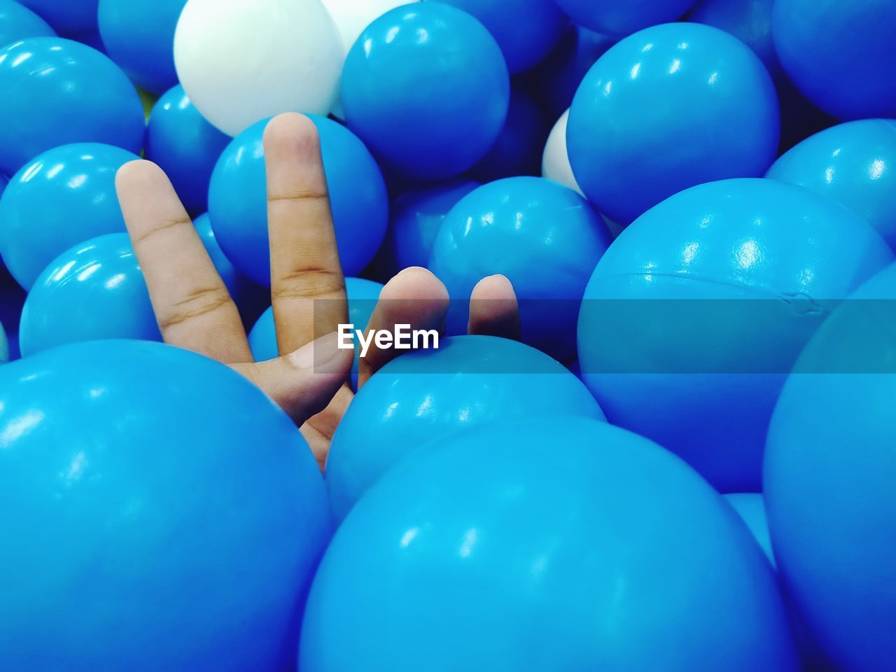 Cropped hand gesturing peace sign amidst blue balls