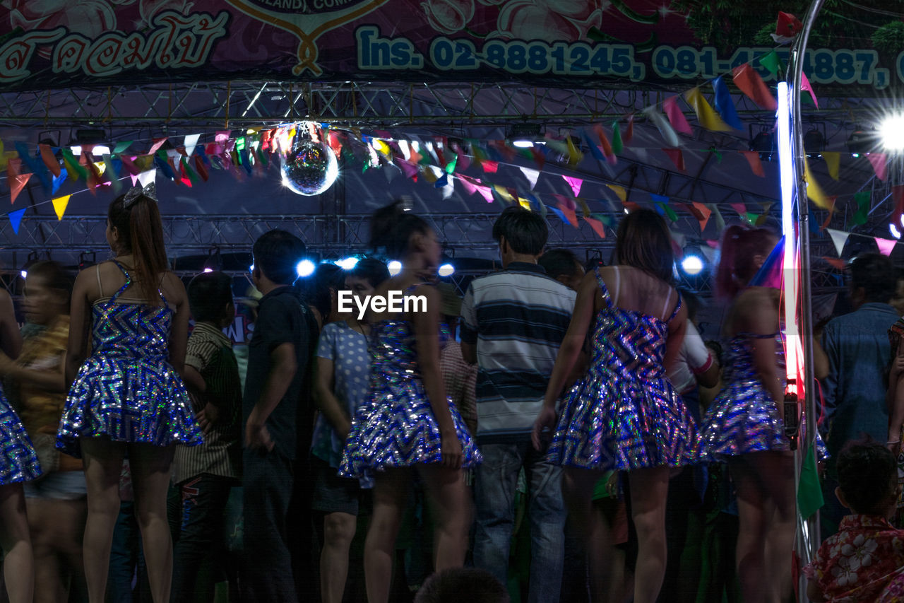 REAR VIEW OF PEOPLE STANDING AT ILLUMINATED MARKET