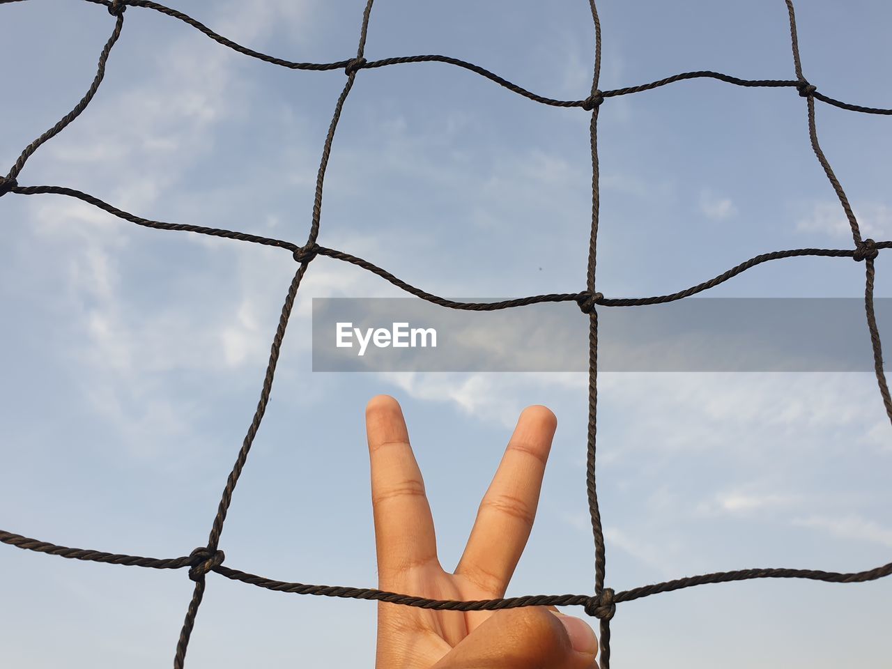 Low angle view of hand behind tennis net against sky