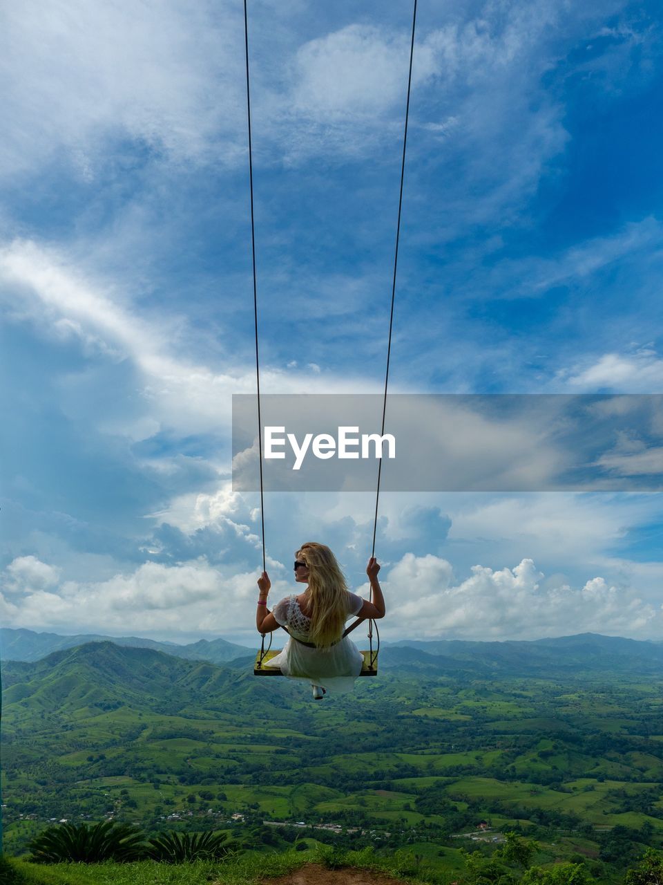 Rear view of woman swinging against landscape and sky