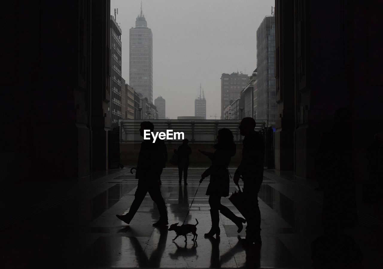 People walking in corridor of building against sky in city