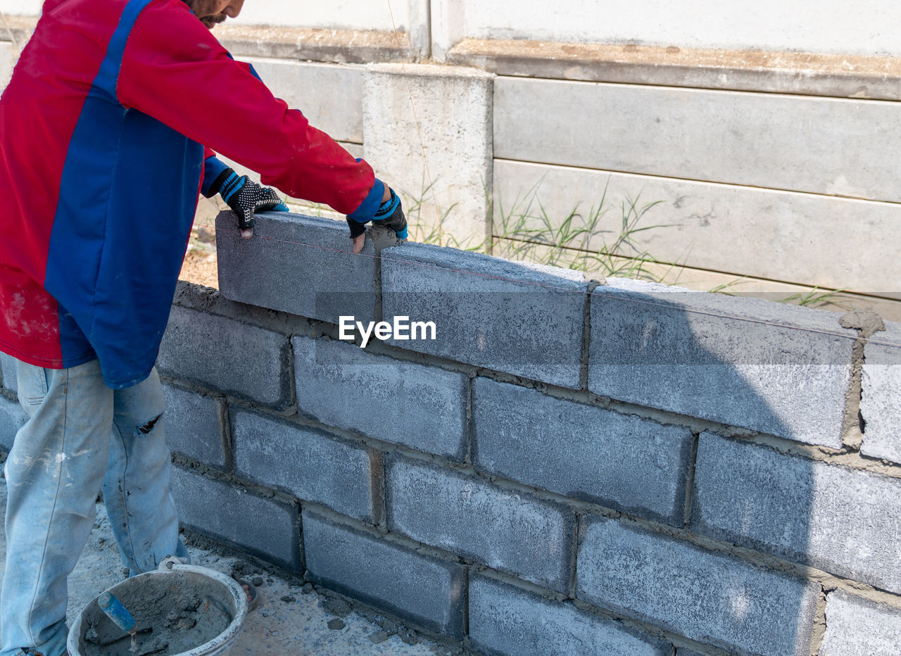 Bricklayer worker installing brick masonry on exterior wall in building site.