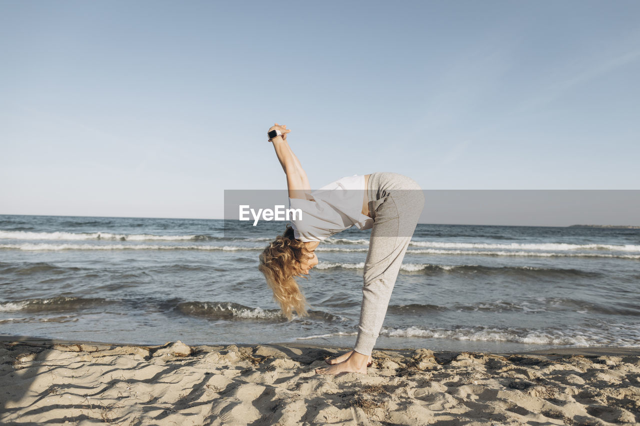 Woman with blond hair practicing stretching exercise on beach